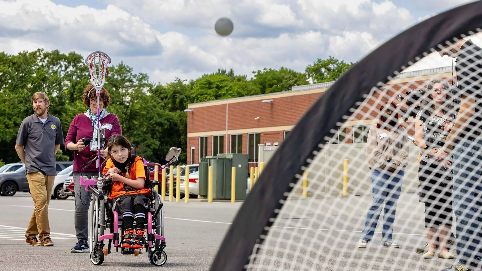Stella Stakolosa launches a ball into the net using an adaptive lacrosse stick designed by College Park Academy students, led by teacher Brendan McCarthy (left), as part of the Engineering for Us All program.